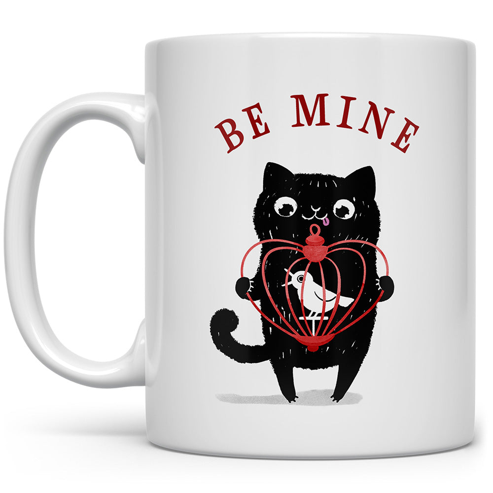 A mug that says Be Mine with a cat holding a birdcage shaped like a heart with a bird inside