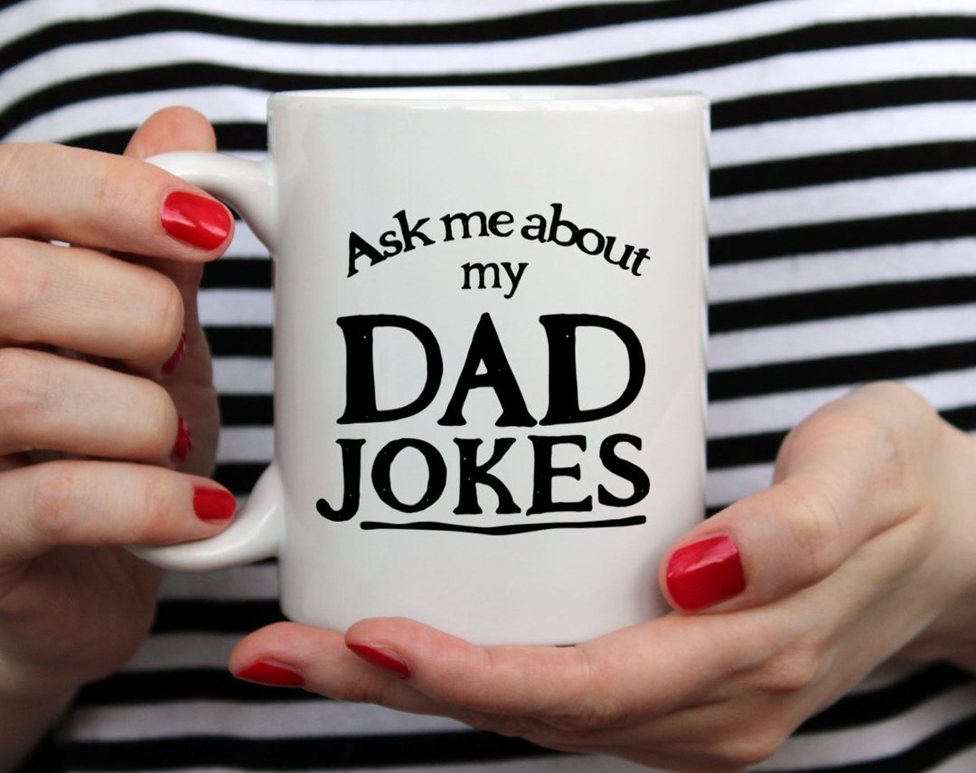Ask Me About My Dad Jokes Mug Gift being held by woman in black and white striped top with red nail polish
