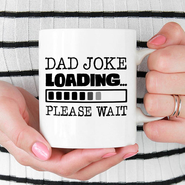 Dad Joke Loading Mug being held by person wearing black and white top with pink nail polish