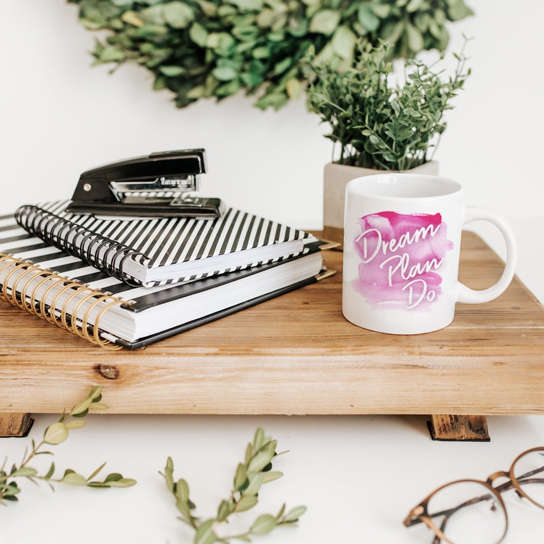 Dream Plan Do Mug on a desk with journals and a stapler next to it