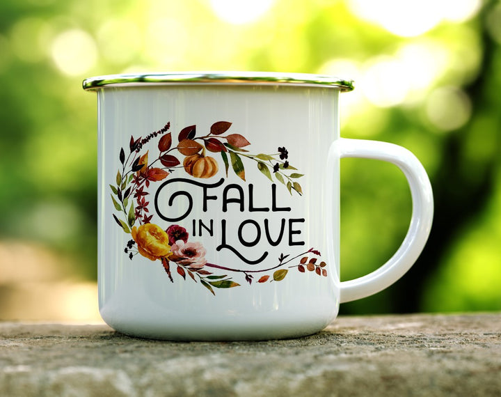 White mug that says Fall in Love with fall flowers and squash on it on a log
