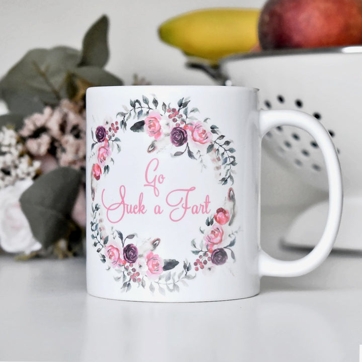 mug that says Go Suck a Fart on a kitchen counter with fruit in the background