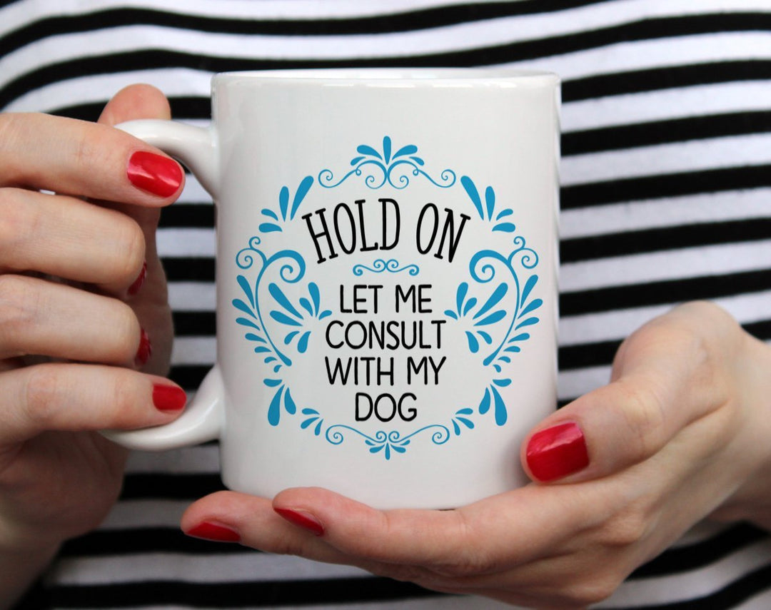 Mug that says Hold On Let me Consult with my Dog with blue doodles being held by woman wearing black and white top with red nail polish