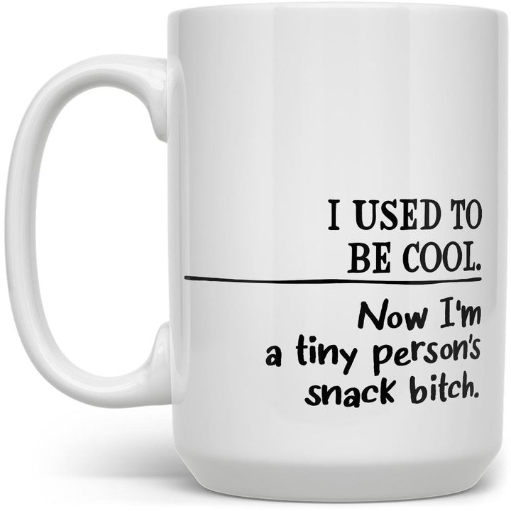white mug that says I used to be cool, now I'm a tiny person's snack bitch on a white background