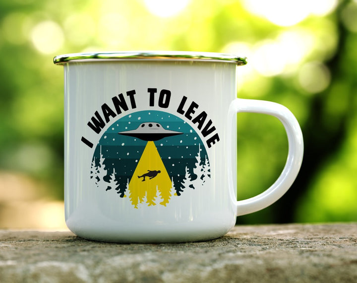 a white camp mug that says I want to leave with UFO pulling a person up to it on a log