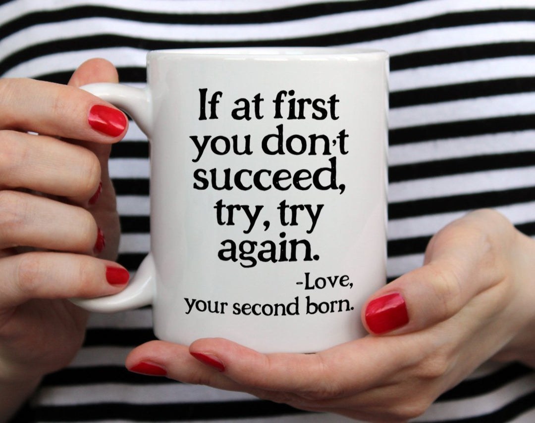 Mug that says If at first you don't succeed, try, try again - Love, your second born being held by woman wearing black and white top with red nail polish