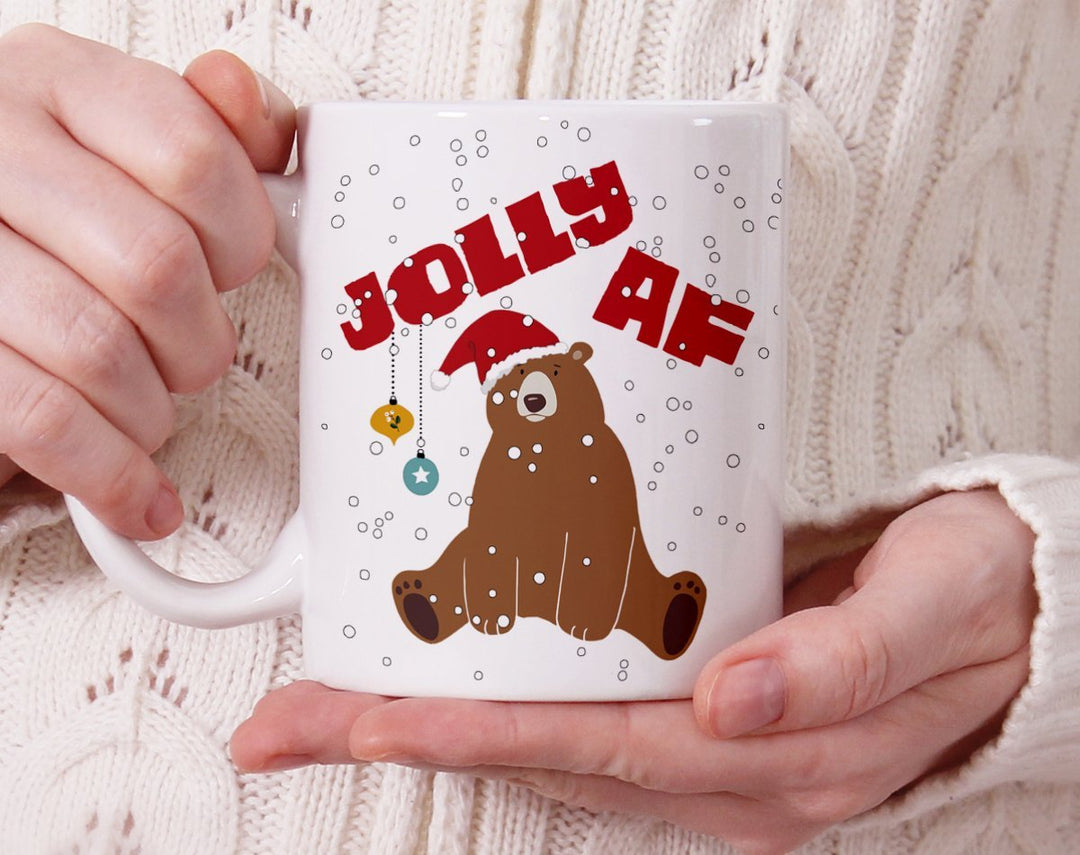 Mug that says Jolly AF with a sad bear in a santa hat being held by a person
